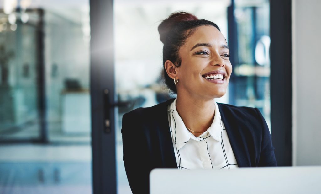 A confident young businesswoman smiles as she works at her desk in a modern office.