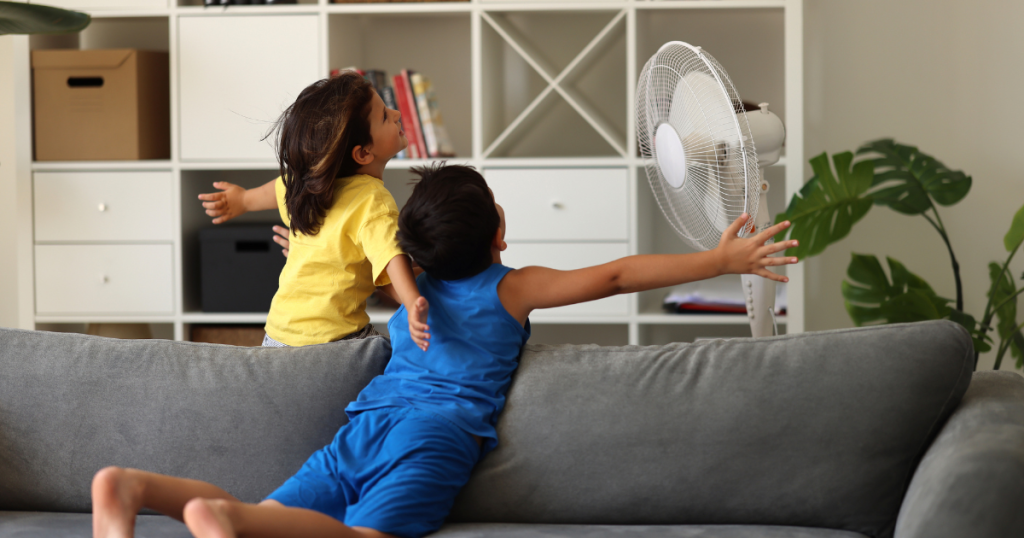 Two young children in front of a fan on a hot summer day.