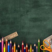 Various school supplies arranged on chalkboard green background