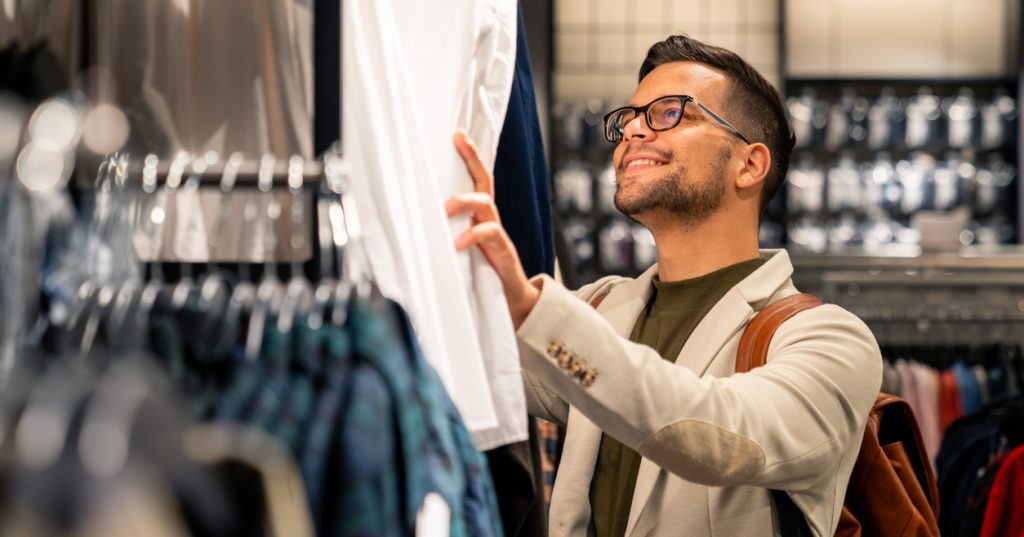 A customer in casual attire examines a shirt while shopping at a contemporary clothing store with organized retail displays.