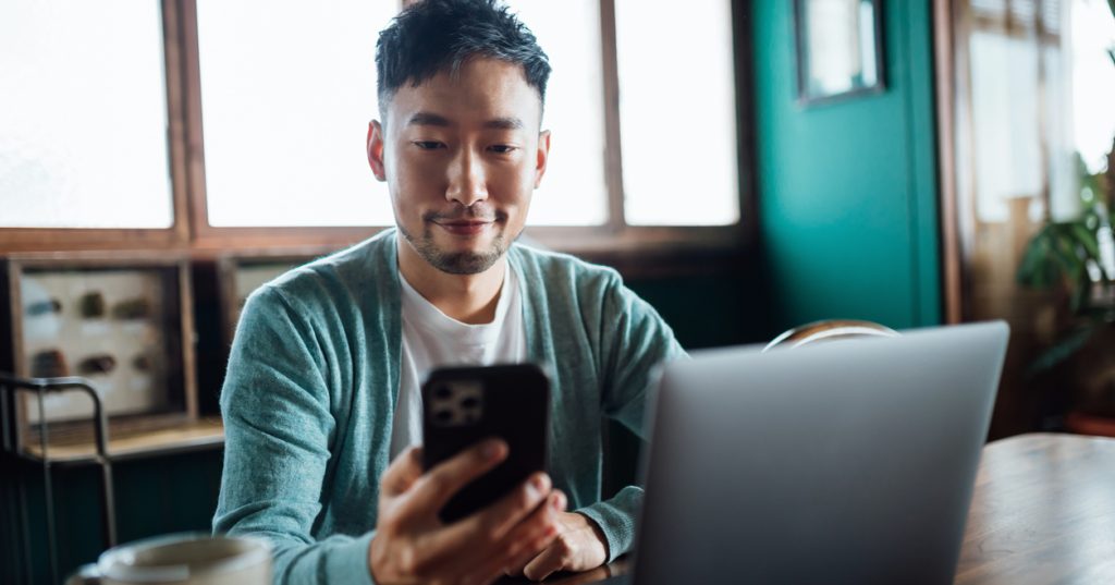 Man looking at smartphone while working on laptop computer at kitchen table