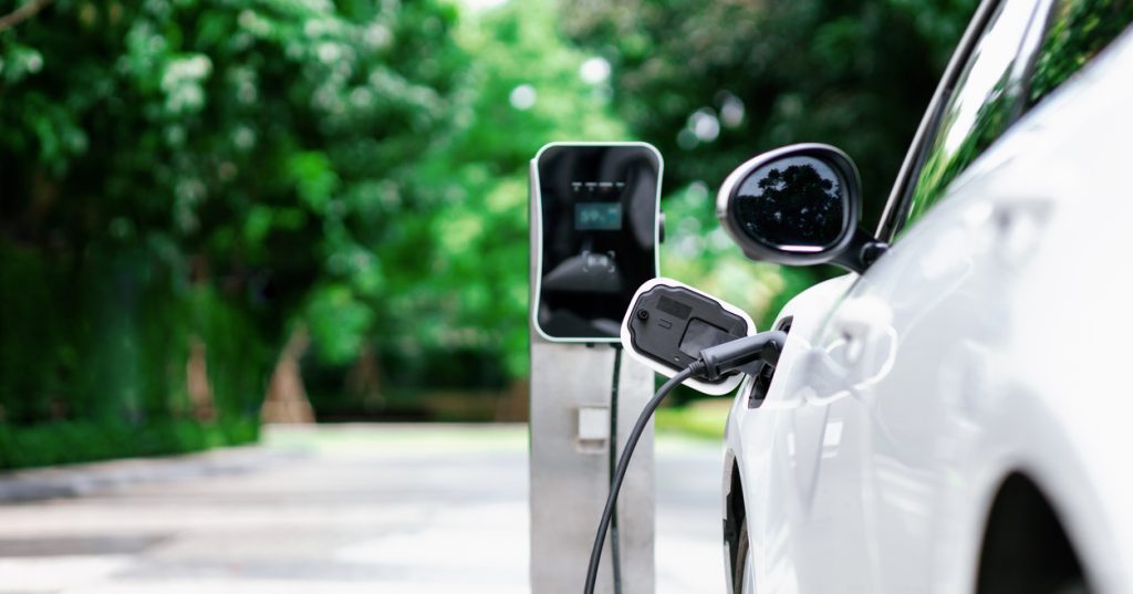 Focus closeup of an electric vehicle plugged into a home EV charger device with blurred background of driveway.