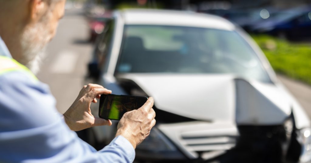A man inspects and photographs his crashed car after a traffic accident.