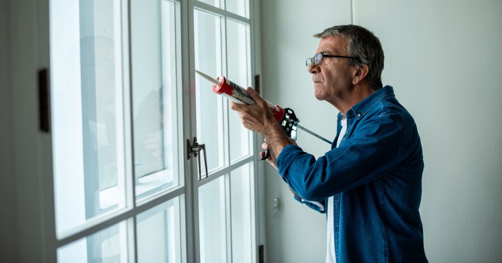 A man seals his window with caulk.