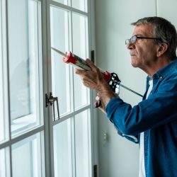 A man seals his window with caulk.